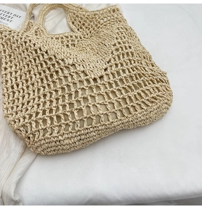 Detail shot of a beige hollow straw tote bag with woven handles on white fabric