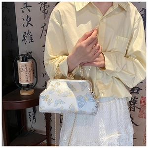 Détail du sac à main en soie bleue avec jacquard papillon doré et poignée métallique