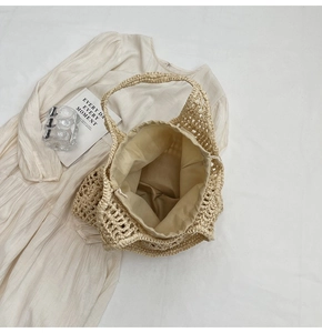 Flat lay of beige woven tote bag with drawstring lining on a white dress for summer