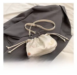 Close-up of ivory silk crossbody bag featuring elegant floral embroidery and drawstring detail