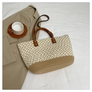Flat lay of a bohemian hand-woven tote bag with leather handles on a white fabric surface
