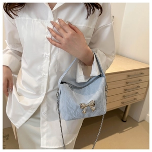 Détail du sac en similicuir bleu clair avec nœud en métal argenté et texture plissée