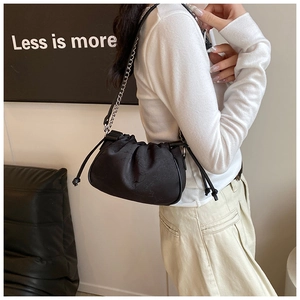 Detail of black pleated cloud bag with drawstring closure and mixed chain strap on model