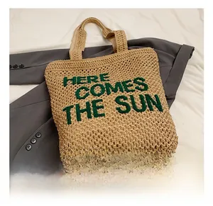 Detail of straw tote bag featuring green Here Comes The Sun embroidery and woven texture