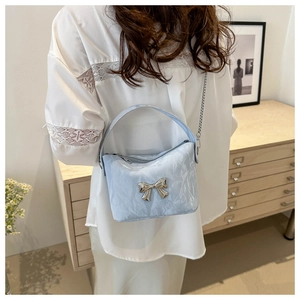 Détail du sac plissé bleu clair en PU avec nœud argenté et chaîne sur un meuble