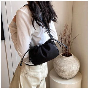 Detail of black pleated cloud bag with drawstring closure and metal chain shoulder strap