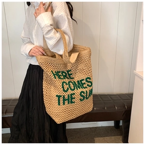 Straw tote bag detail with green embroidered text Here Comes The Sun and woven texture