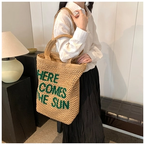 Detail view of woven straw tote bag with green Here Comes The Sun embroidery on shoulder