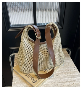 Detail of woven straw bag with brown leather strap and golden buckle on a book