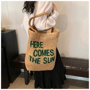Detail of straw shoulder tote with green Here Comes The Sun embroidery for summer