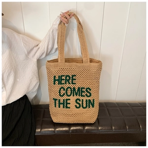 Detail of woven straw tote bag with green Here Comes The Sun embroidery on natural fiber