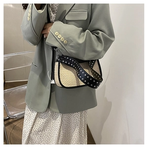 Détail du sac bandoulière en paille tissée avec sangle en cuir noir ornée de clous argentés