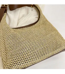 Close-up detail of woven straw tote bag with brown leather trim and wide shoulder strap