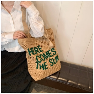 Detail of straw tote bag with green embroidered Here Comes The Sun text and wide strap
