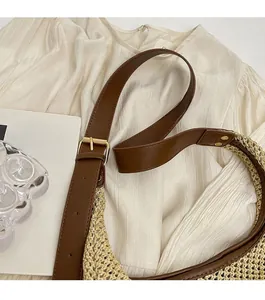 Detail of adjustable brown leather strap and gold buckle on a stylish straw crossbody bag