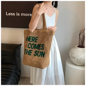 Detail showing handwoven straw texture and Here Comes The Sun text on summer tote