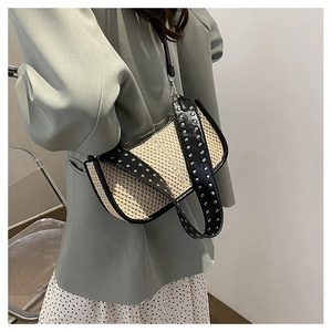 Détail du sac croissant tissé avec bordure en cuir noir et rivets argentés sur modèle
