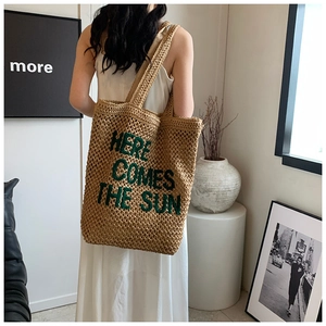 Detail of straw woven tote bag featuring green Here Comes The Sun embroidery