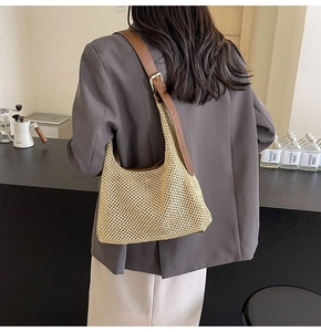 Close-up of handmade straw shoulder bag with dark brown leather strap and metal buckle