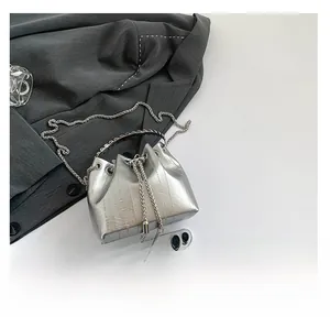 Mini silver metallic bucket bag with chain strap shown next to phone for size reference