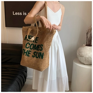 Detail of straw tote bag with green embroidered text worn with white dress
