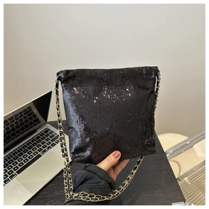 Fashionable black sequin crossbody bag with chain strap on a dark desk with laptop