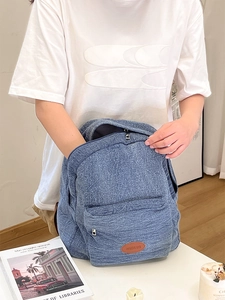 Detail of blue denim backpack showing front zipper pocket and brown leather logo tag