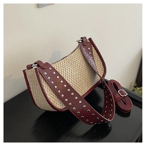 Détail du sac demi-lune en paille tressée avec bordure en cuir rouge et rivets argentés