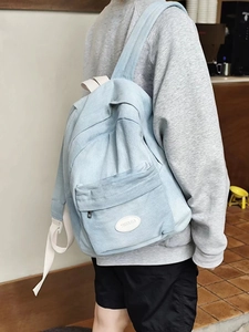 Detail shot of light blue denim backpack with white straps and minimalist oval logo patch