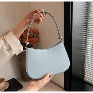 Minimalist light blue leather underarm bag with smooth curved design held by model