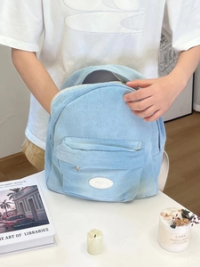 Close-up of light blue denim backpack showing front zipper pocket and white brand patch