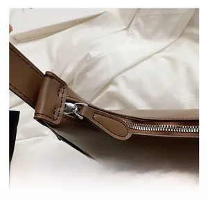 Detailed close-up of a brown leather shoulder bag featuring a smooth silver zipper closure