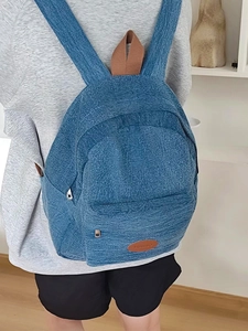Close-up of blue denim texture backpack featuring brown woven handle and leather logo patch