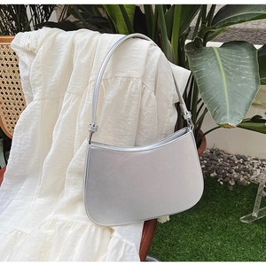Close-up of the silver metallic half-moon shoulder bag on a white dress and rattan chair
