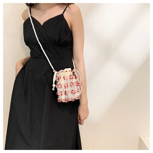 Detail of a handmade beaded mini crossbody bag with red floral accents and pearl strap