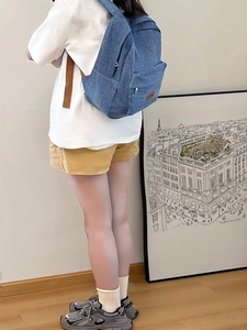 Deep blue denim backpack featuring a brown leather logo tag worn by a model in a stylish room