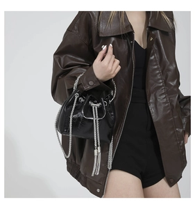Detail of glossy black mini bucket bag with silver chain handle on leather jacket model