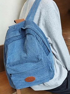 Detailed view of durable denim fabric texture and brown leather logo patch on backpack