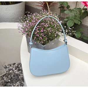 Close-up of minimalist light blue shoulder bag with matte leather finish on a white surface