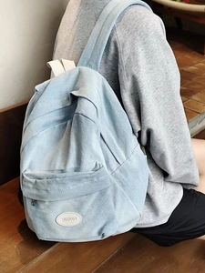 Detail shot of light blue denim backpack showing wash fabric texture and brand patch