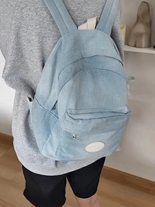 Rear view of model wearing a light blue washed denim backpack with a logo patch