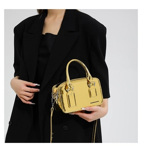 Detail view of metallic gold cross-body bag with zipper and detachable strap on black blazer