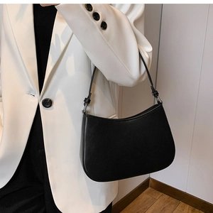 Close-up of minimalist black leather hobo bag worn with a chic white blazer and black outfit