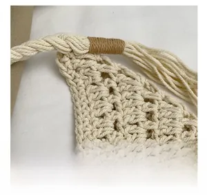 Detail of hollow woven cream handbag showing knotted cotton handle and tassel accents