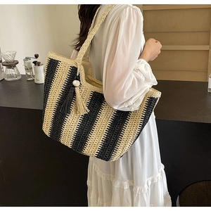 Detail of hand-woven straw tote with black and beige stripes, tassels, and braided shoulder strap