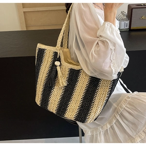 Close-up of woven straw tote bag with black and yellow stripes and fringe tassel detail