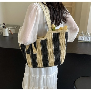 Close-up of woven straw tote bag with vertical stripes and tassel on a female model