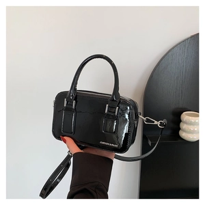 Minimalist black patent leather crossbody bag with silver lettering on white background