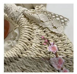Détail du sac en paille tressée beige avec broderie florale rose et bordure en dentelle