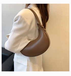 Detail of a dark brown half-moon PU leather shoulder bag with circular buckle on a model